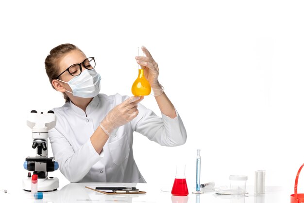 Вид спереди женщина-врач в медицинском костюме в маске из-за covid, работающего с растворами на белом пространстве