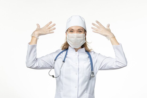 Front view female doctor in medical suit wearing mask and gloves due to coronavirus on the light desk disease virus covid- pandemic disease illness