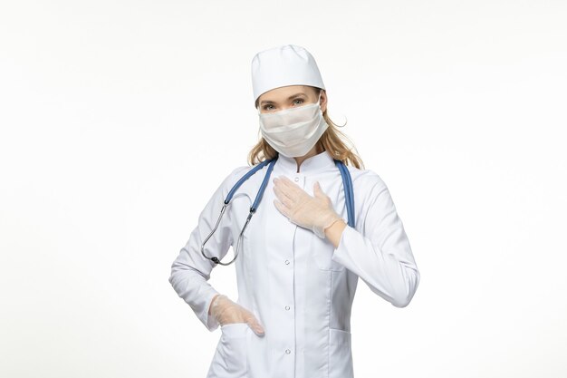 Front view female doctor in medical suit wearing mask and gloves due to coronavirus on light wall disease virus covid- pandemic disease illness