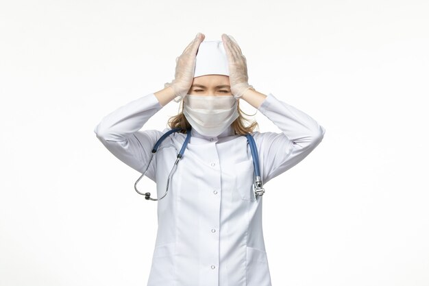 Front view female doctor in medical suit wearing mask and gloves due to coronavirus on light wall disease virus covid- pandemic illness