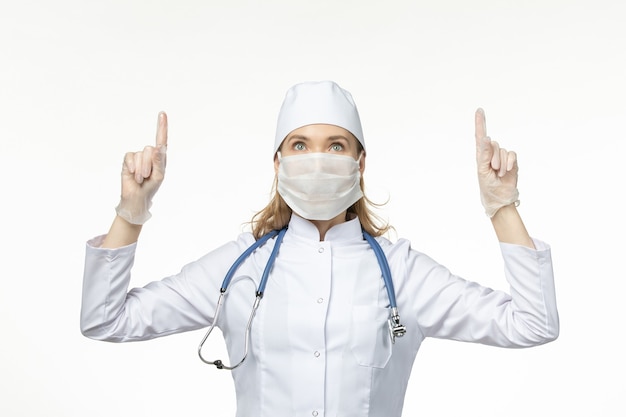 Front view female doctor in medical suit wearing mask and gloves due to coronavirus on light wall disease virus pandemic disease illness