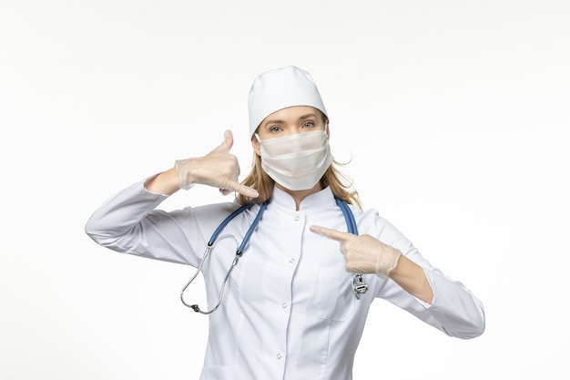 Front view female doctor in medical suit wearing mask and gloves due to coronavirus on light white desk pandemic covid- disease virus