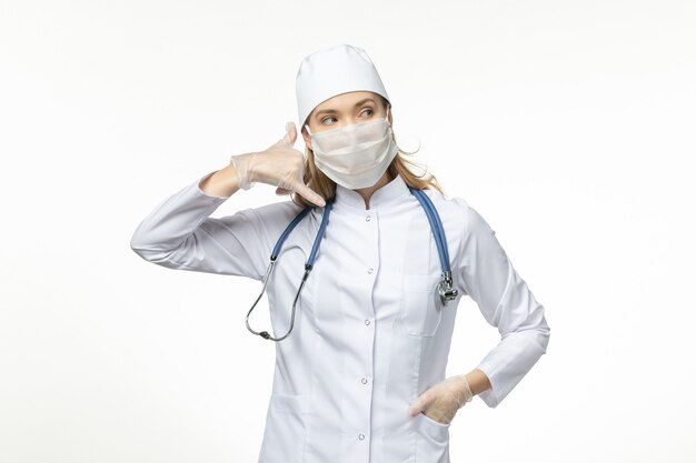 Вид спереди женщина-врач в медицинском костюме в маске и перчатках из-за телефонного звонка из-за коронавируса позы на белом столе вируса пандемического заболевания