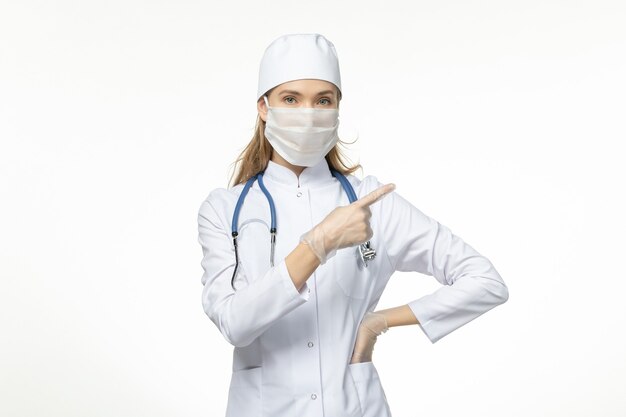 Front view female doctor in medical suit wearing mask and gloves due to coronavirus on white desk disease covid- pandemic disease illness