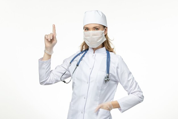 白い壁にコロナウイルスが原因でマスクと手袋を着用した医療スーツを着た女性医師の正面図パンデミック病ウイルス病