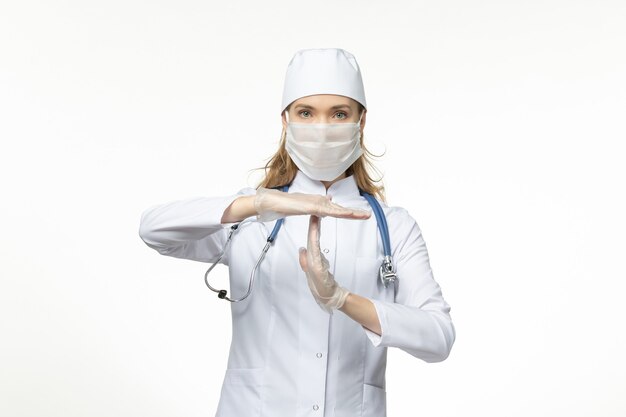 Front view female doctor in medical suit wearing mask and gloves due to coronavirus on white wall pandemic covid- disease virus