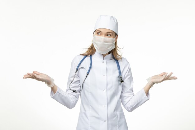 白い壁の病気のパンデミックコビッドのコロナウイルスのために手袋をはめたマスクを身に着けている医療スーツの正面図の女性医師-