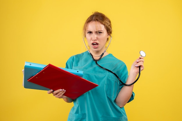 Front view of female doctor in medical suit with analysis and stethoscope on yellow wall