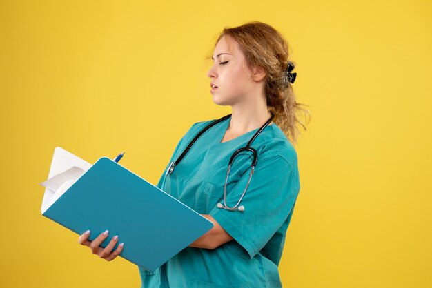 Front view of female doctor in medical suit with analysis on yellow wall