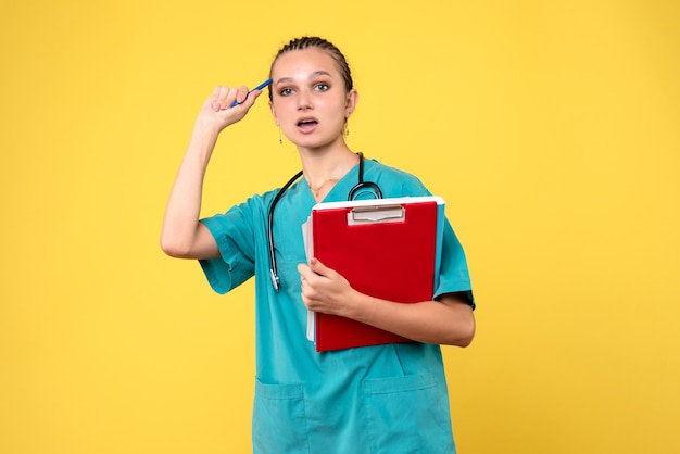 Front view of female doctor in medical suit with different analysis on a yellow wall