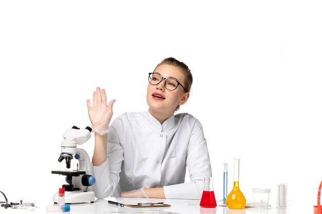 Front view female doctor in medical suit with gloves sitting with solutions on the white space