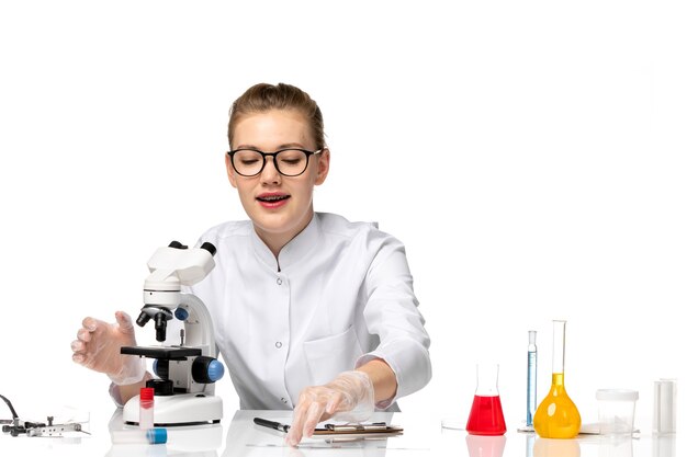 Front view female doctor in medical suit with gloves in working process on white desk