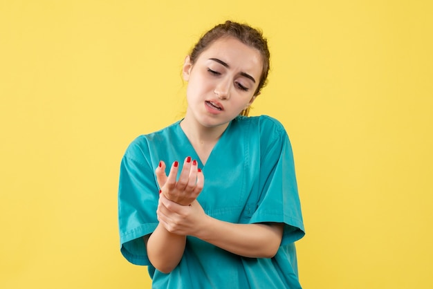 Front view of female doctor in medical suit with hurt arm on yellow wall