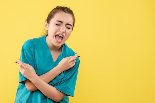 Vista frontale della dottoressa in tuta medica con braccio danneggiato sulla parete gialla