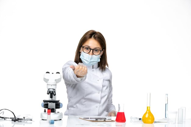 Front view female doctor in medical suit with mask due to covid calling on a white space