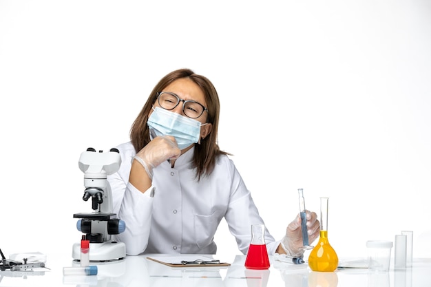 Front view female doctor in medical suit with mask due to covid thinking on white space