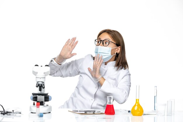 Front view female doctor in medical suit with mask due to covid on a white space