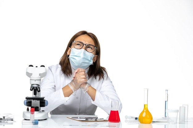 Front view female doctor in medical suit with mask due to covid working and thinking on a white space