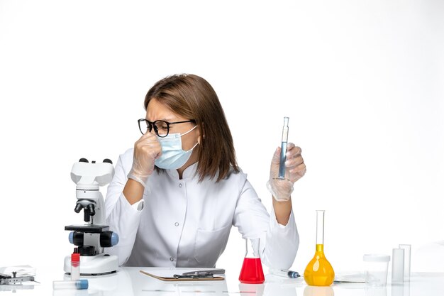 Front view female doctor in medical suit with mask due to covid working with solutions on light-white space