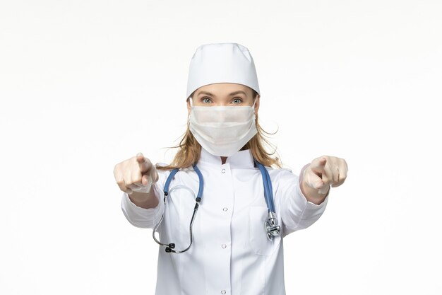 Free photo front view female doctor in medical suit with mask and gloves due to coronavirus on the light white desk disease pandemic covid- virus