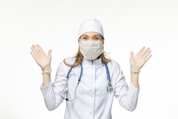 Front view female doctor in medical suit with mask and gloves due to coronavirus on white desk illness pandemic health covid- virus