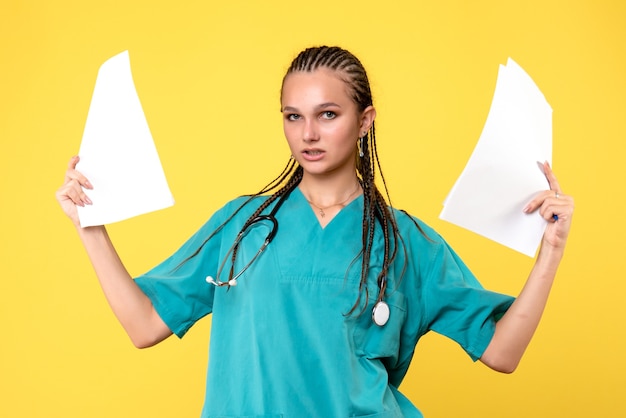 Vista frontale della dottoressa in tuta medica con documenti sulla parete gialla