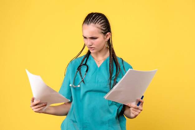 Вид спереди женщины-врача в медицинском костюме с бумагами на желтой стене