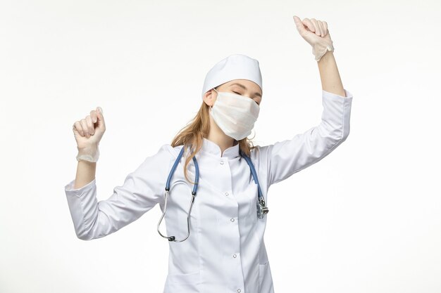 Front view female doctor in medical suit with sterile mask due to coronavirus dancing on white wall illness pandemic health covid-