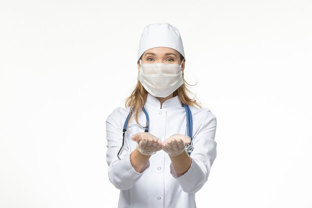 Front view female doctor in medical suit with sterile mask due to coronavirus on white wall illness health covid-