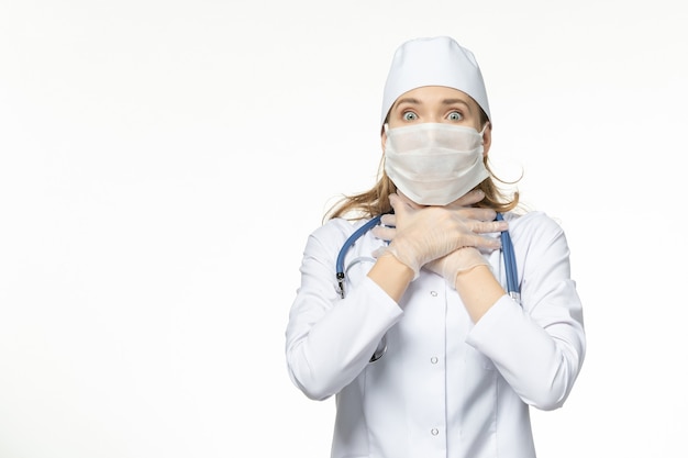 Front view female doctor in medical suit with sterile mask due to coronavirus on the white wall illness pandemic disease covid-