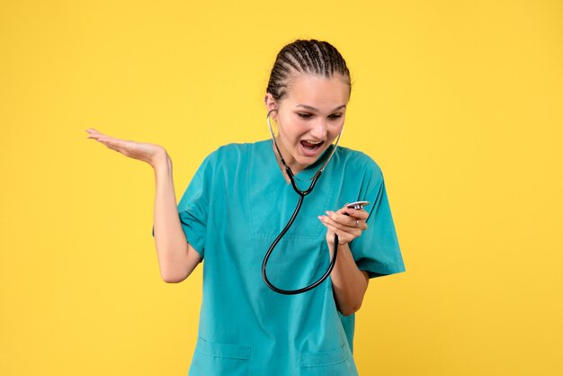 Front view of female doctor in medical suit with stethoscope on a yellow wall