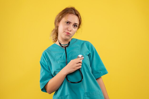 Front view of female doctor in medical suit with stethoscope on yellow wall