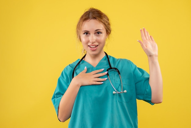 Front view of female doctor in medical suit with stethoscope on yellow wall