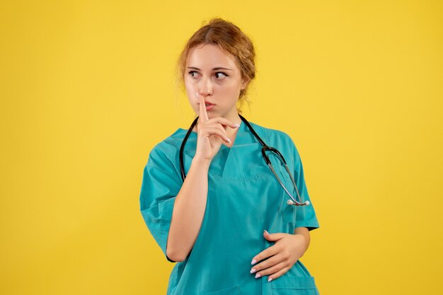 Вид спереди женщины-врача в медицинском костюме со стетоскопом на желтой стене