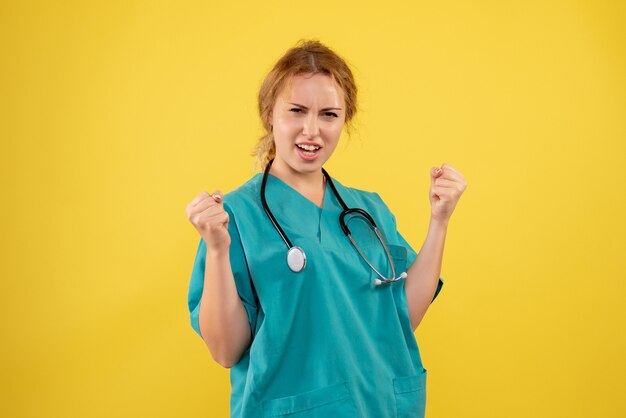 Front view of female doctor in medical suit with stethoscope on yellow wall