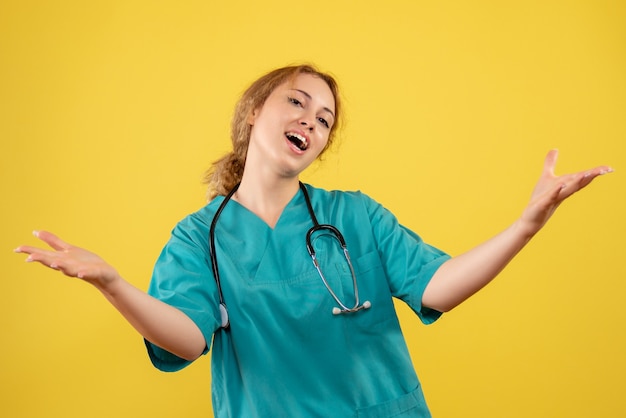 Front view of female doctor in medical suit with stethoscope on yellow wall