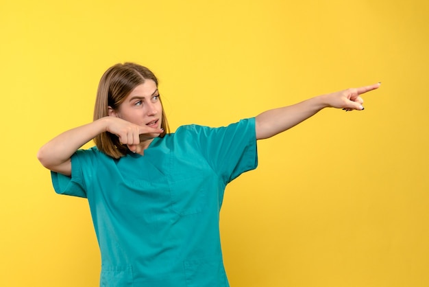 Free photo front view female doctor pointing at distance on yellow space