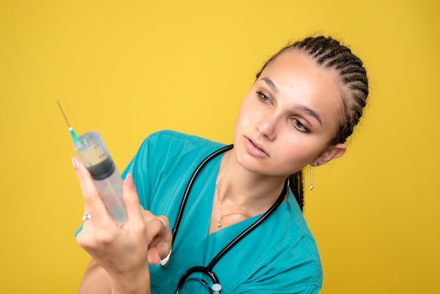 Vista frontale del medico femminile che prepara l'iniezione enorme sulla parete gialla