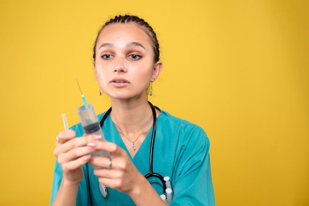 Front view of female doctor preparing huge injection on yellow wall