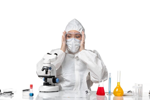 Front view female doctor in protective suit with mask due to covid scared to use microscope on a white background virus pandemic splash covid-