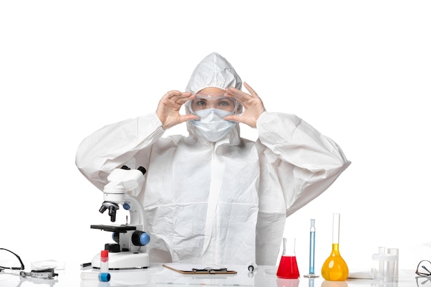 ライトホワイトの背景ウイルスパンデミックスプラッシュcovid-に座っているcovidによるマスク付きの防護服の正面図の女性医師
