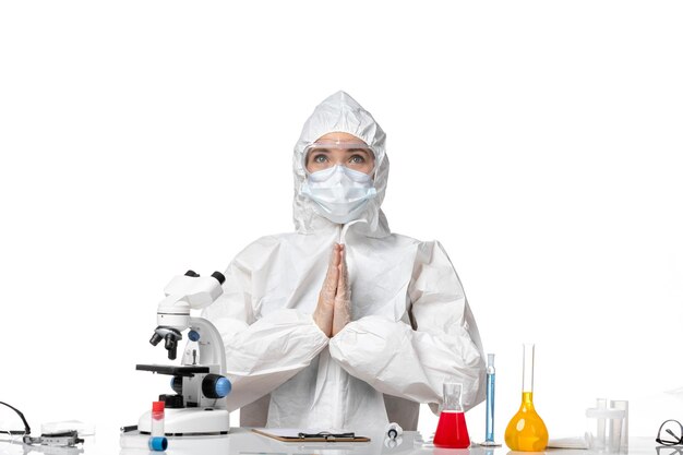 Вид спереди женщина-врач в защитном костюме с маской из-за covid сидит на белом фоне пандемический всплеск вируса covid-