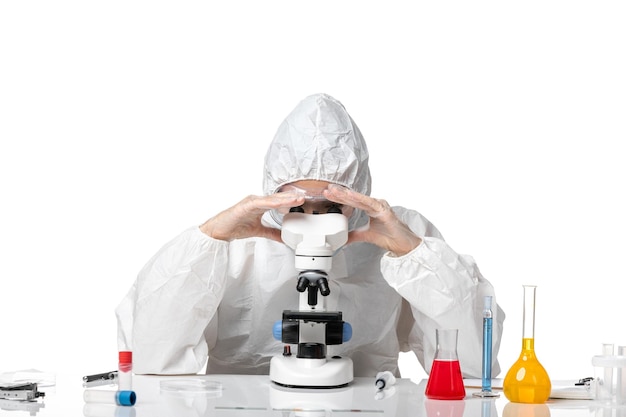 Front view female doctor in protective suit with mask due to covid using microscope on white background virus pandemic health covid