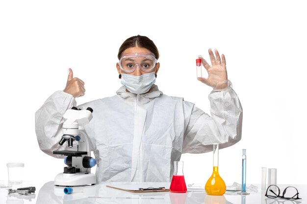 Front view female doctor in protective suit and with mask holding empty flask on light-white background pandemic virus coronavirus covid health