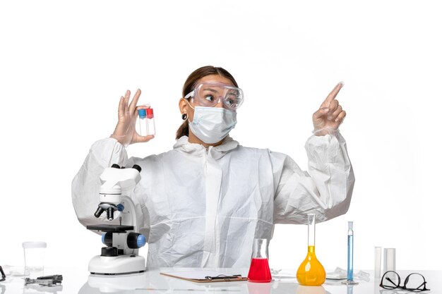 Front view female doctor in protective suit and with mask holding empty flasks on light white background covid health pandemic virus coronavirus