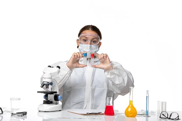 Front view female doctor in protective suit and with mask holding empty flasks on white background covid health pandemic virus coronavirus