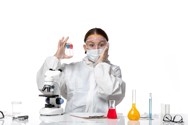 Front view female doctor in protective suit and with mask holding empty flasks on the white background covid pandemic virus coronavirus