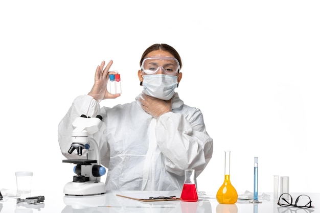 Вид спереди женщина-врач в защитном костюме и с маской, держащая пустые фляги на белом столе, пандемический вирус covid health, коронавирус