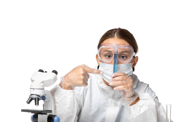 Front view female doctor in protective suit and with mask holding flask with blue solution on light white background covid virus pandemic coronavirus