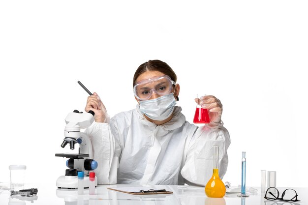 Вид спереди женщина-врач в защитном костюме и с маской, держащая колбу с красным раствором на белом фоне, пандемический коронавирус вируса ковид
